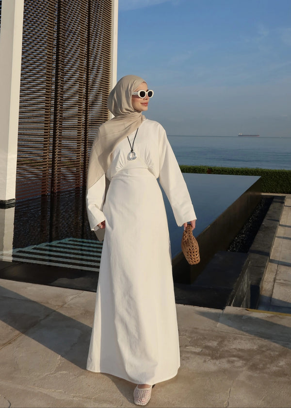 Woman in a white dress with a hijab standing by a pool with ocean view