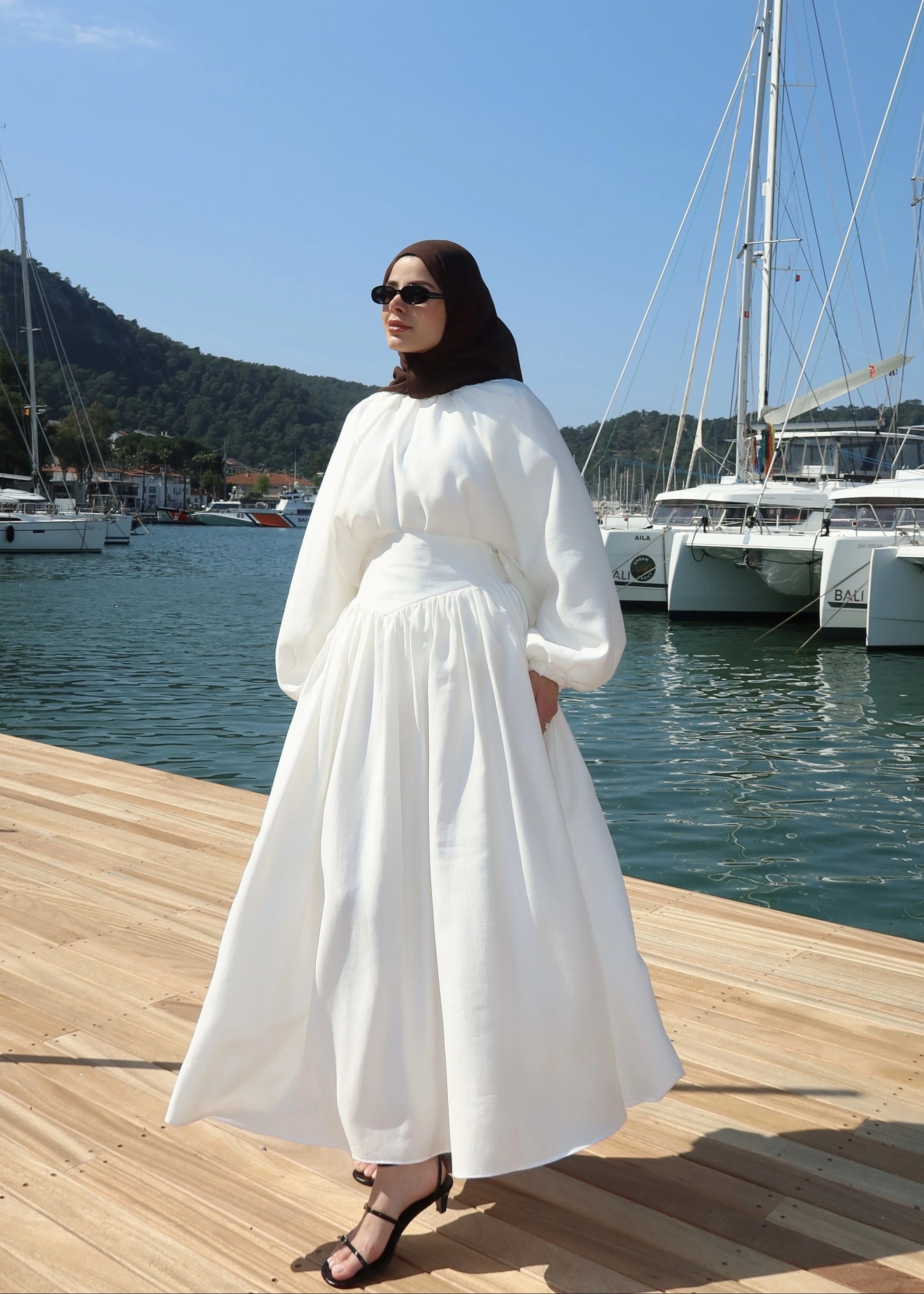 Woman in a white co-ords standing on a dock with boats in the background